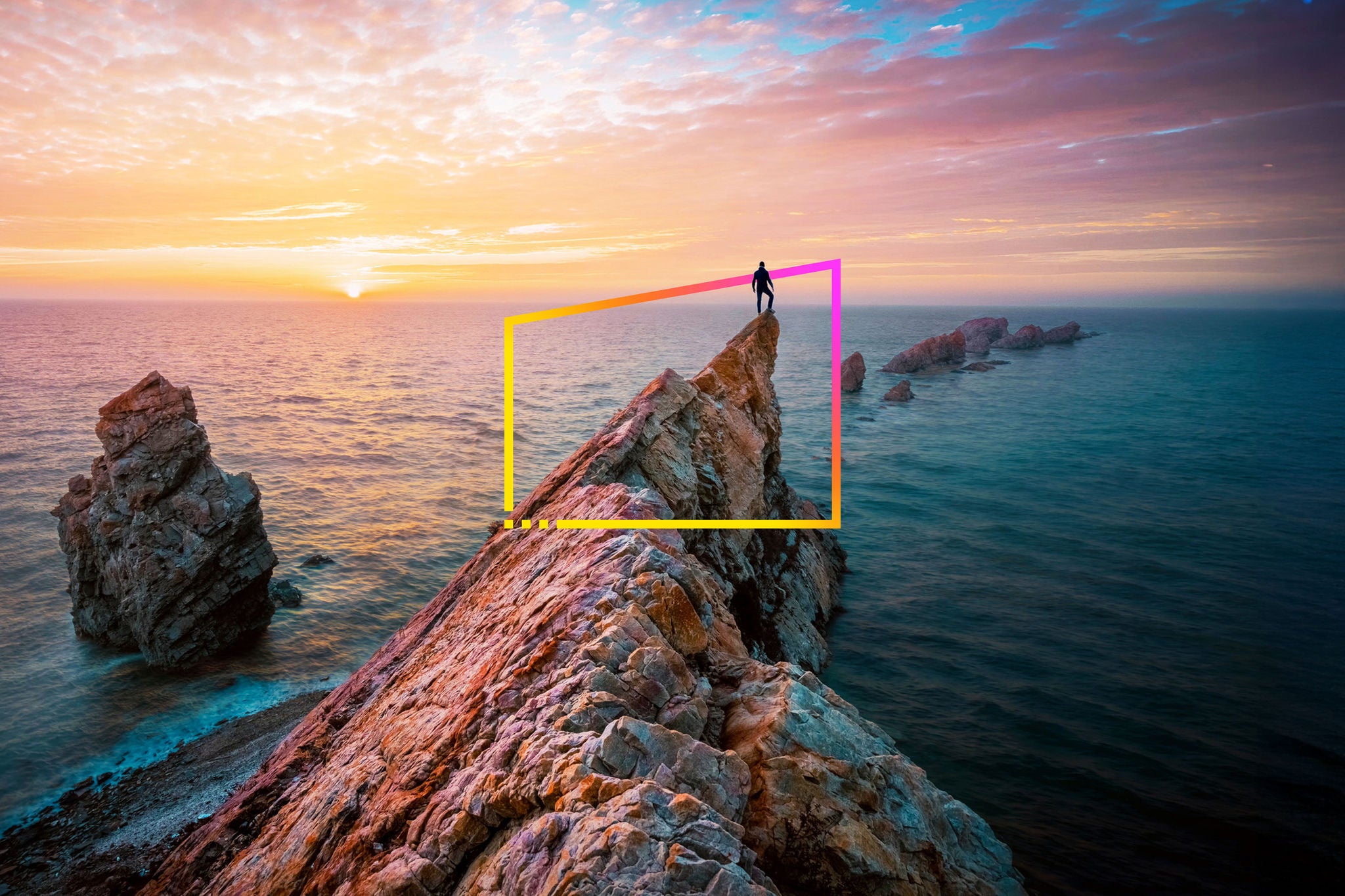 Man standing on rocky outcrop by sea watching sunset 