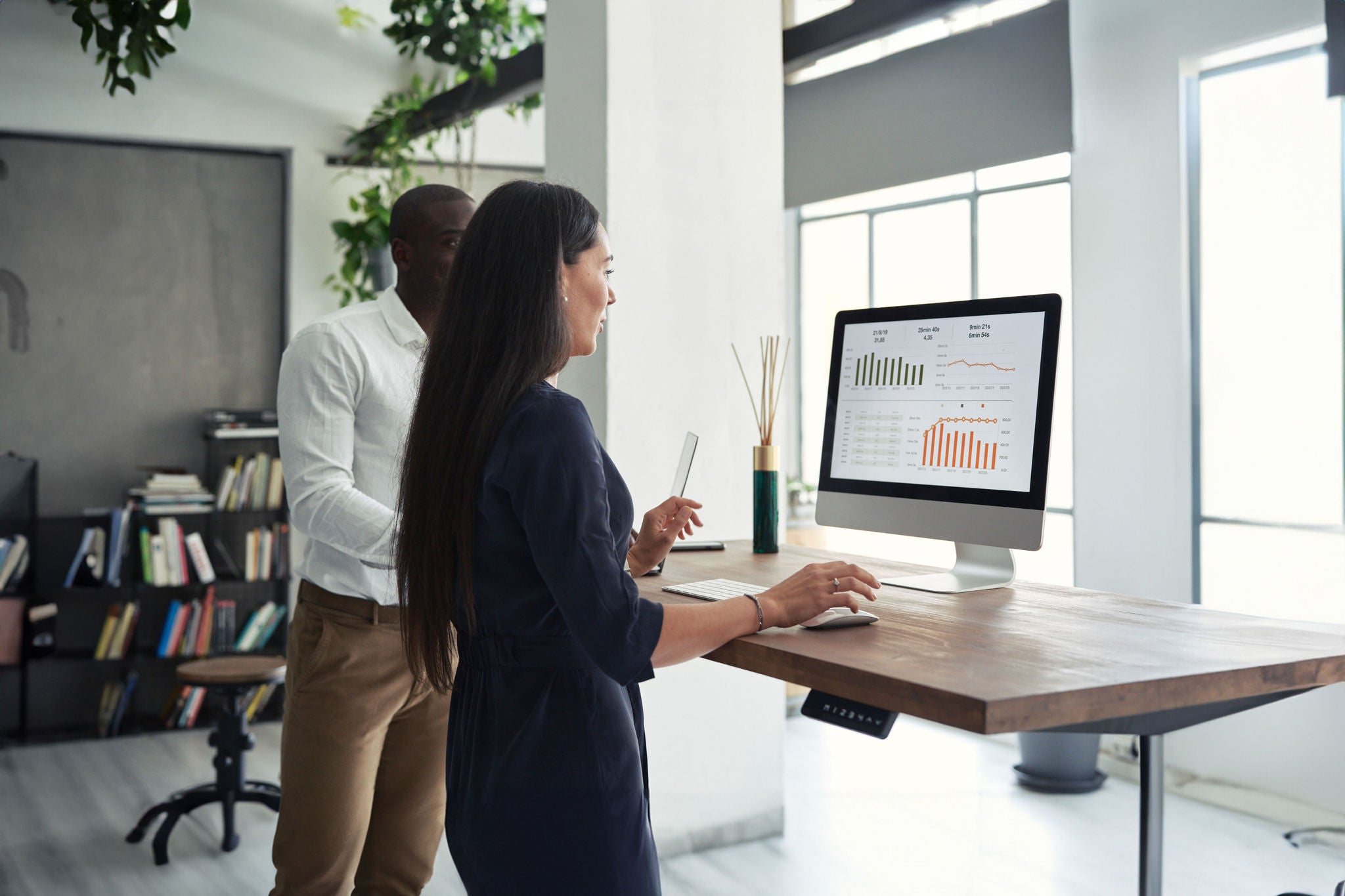 Back view of multiracial man and woman in formal clothes working on desktop computer at counter in office