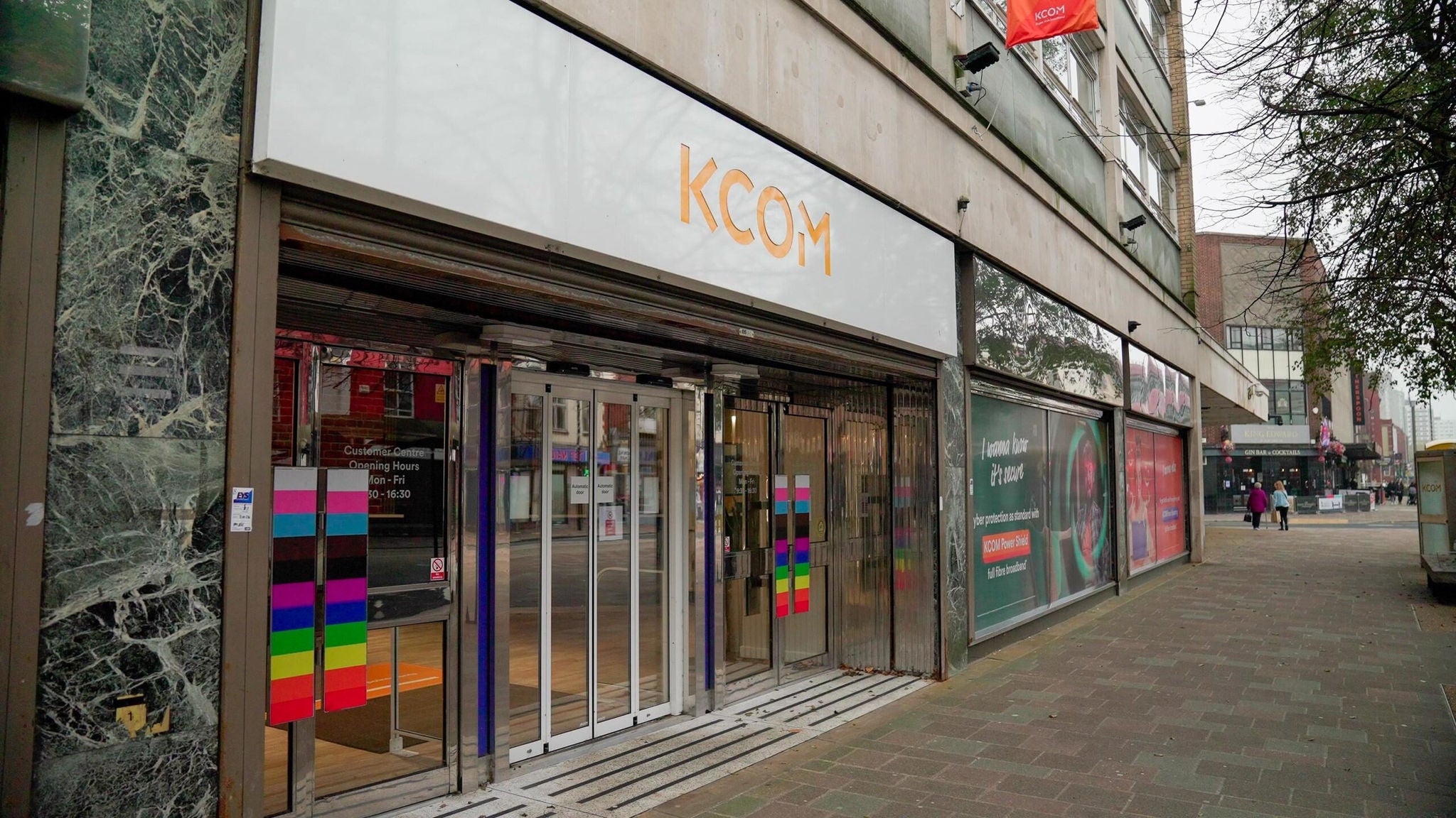 Exterior view of a KCOM customer service centre with glass doors and promotional content about fibre broadband.